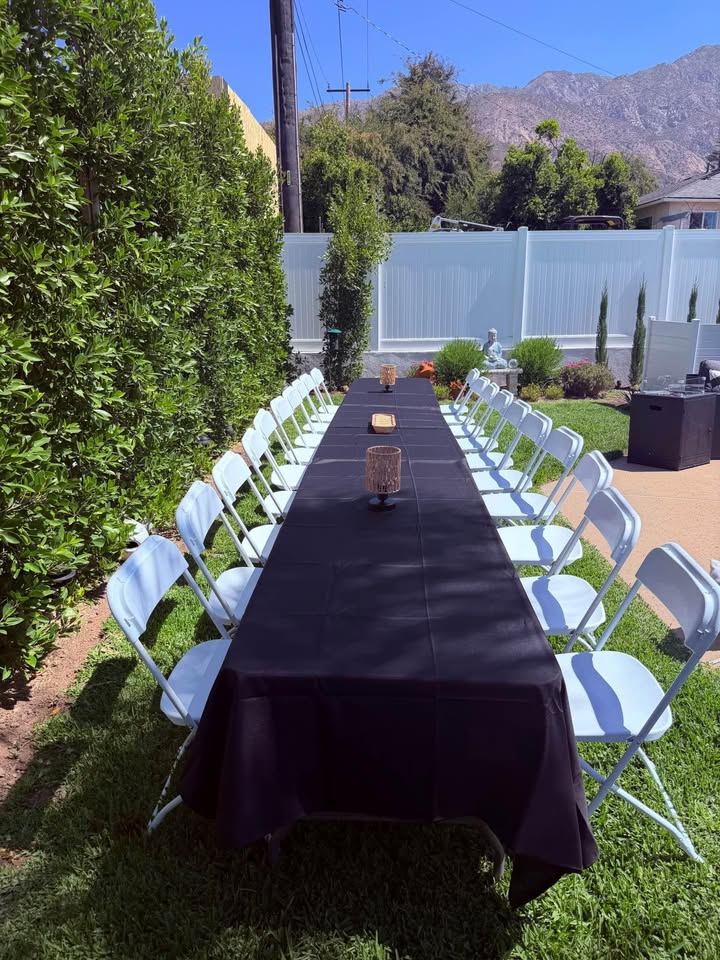 Banquet row with black tablecloths and white folding chairs on grass