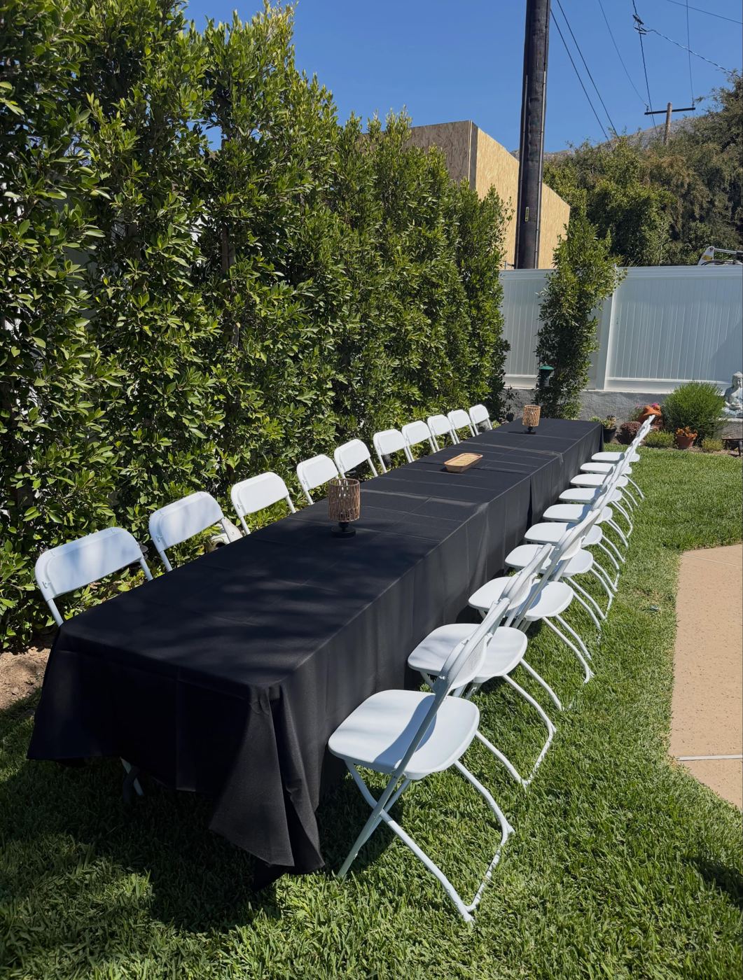 Long banquet row of tables with black tablecloths and white folding chairs on a lawn