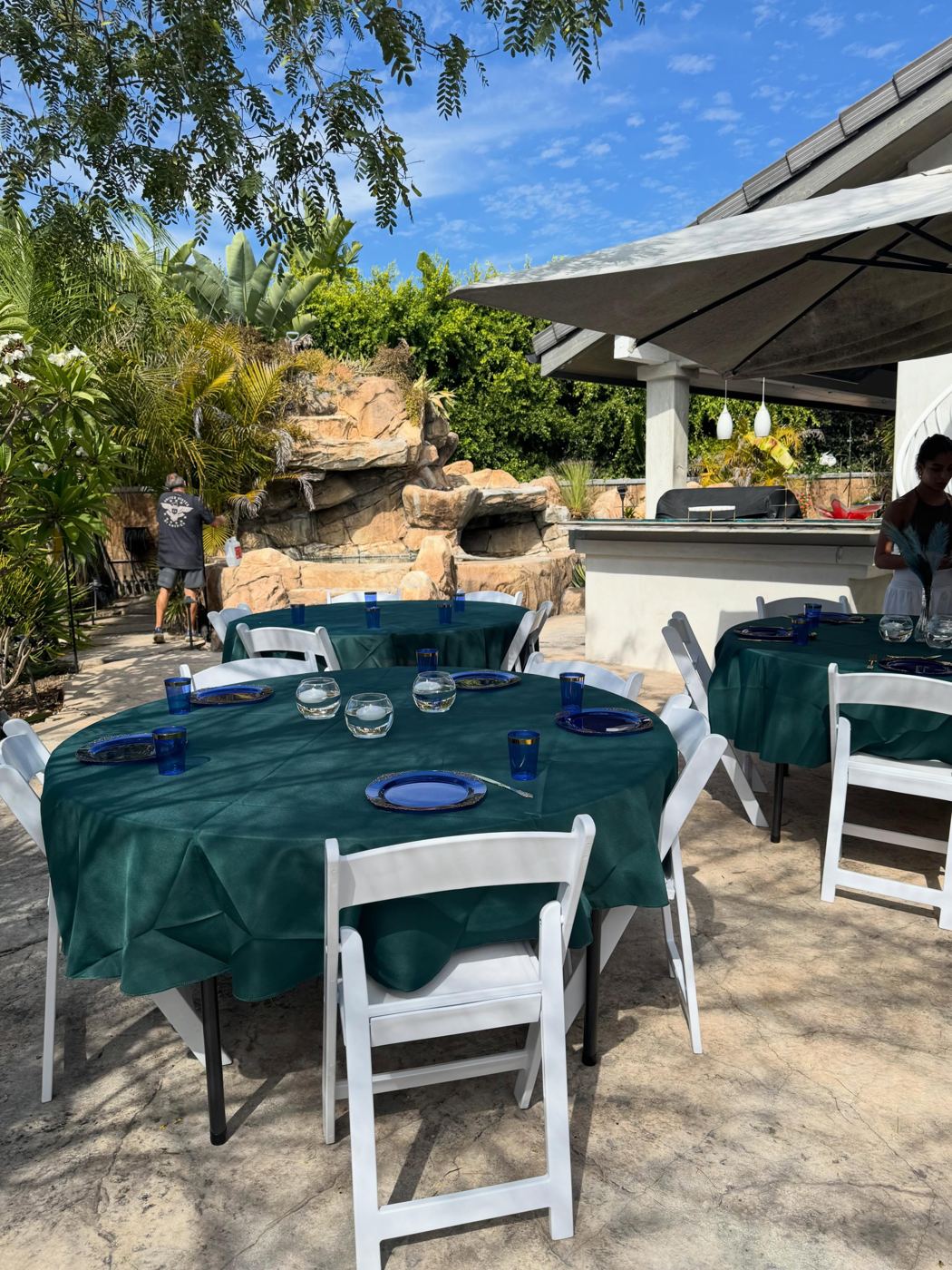 Round tables with emerald linens and white chairs beside an outdoor kitchen