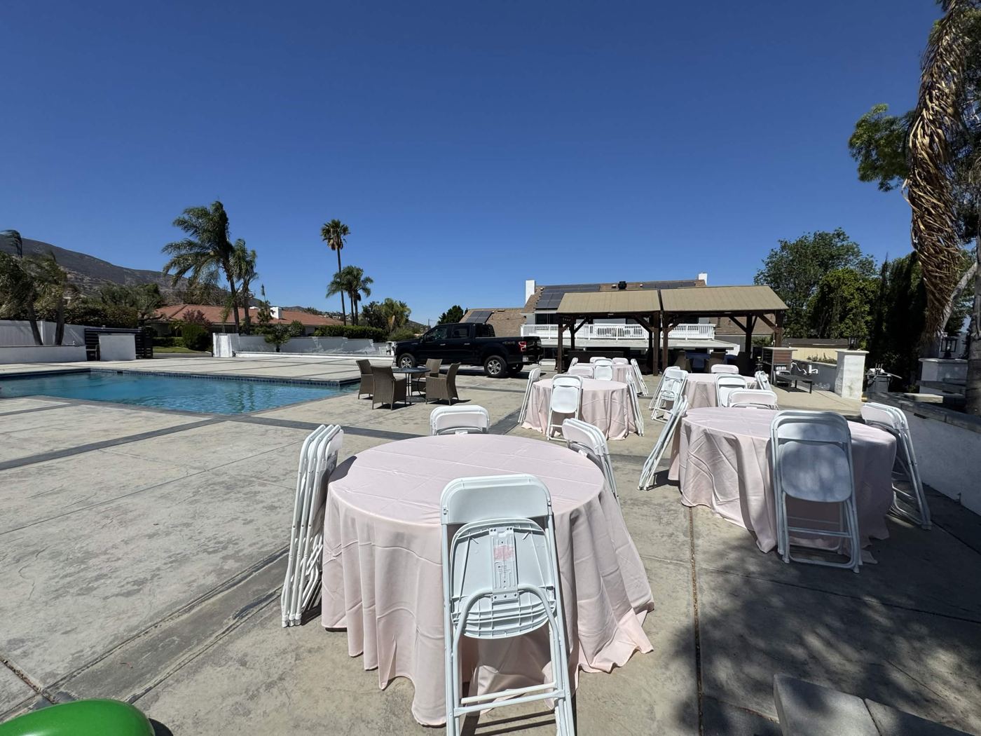 Round tables with blush tablecloths and white chairs next to a pool